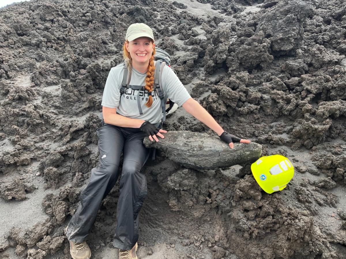 Christelle Wauthier sits on a rough volcanic rock during fieldwork.