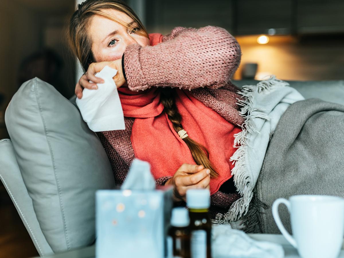 Woman coughing on a sofa and holding a tissue while sick with the flu.