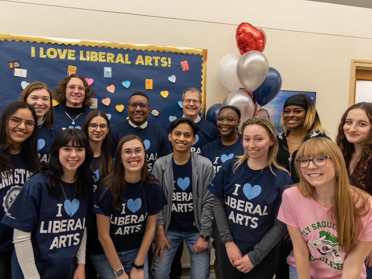 Dean Clarence Lang and Associate Dean Mark Morrisson (center back) with students wearing navy shirts that read “I love Liberal Arts” stand in front of a bulletin board that reads “I love Liberal Arts” in Sparks Building.