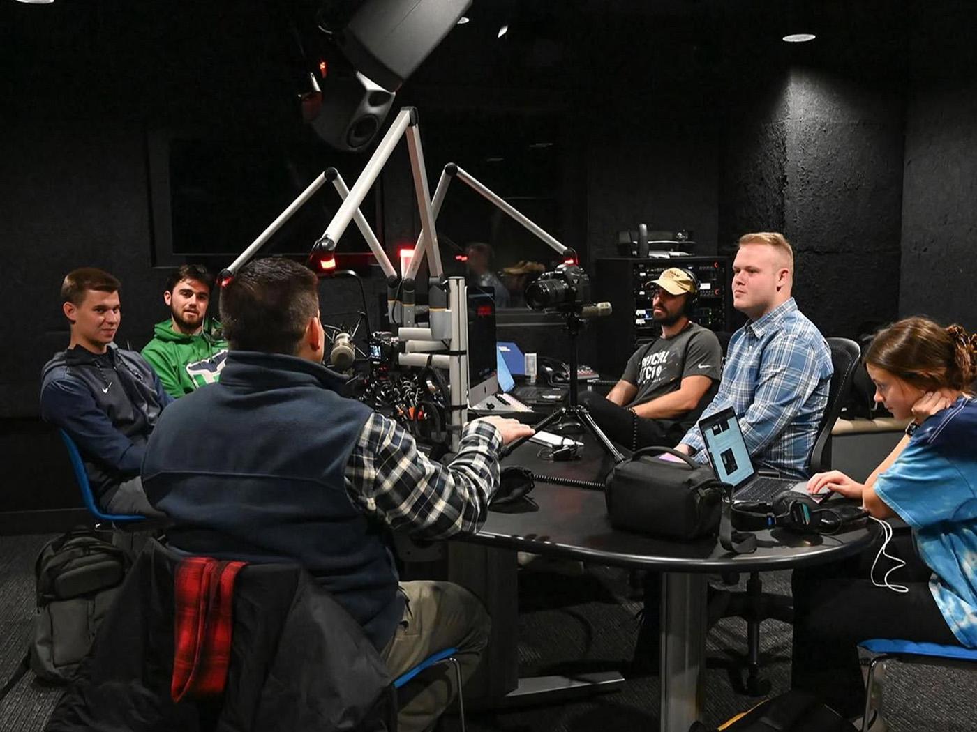 A group of people seated around a table with broadcast microphones.