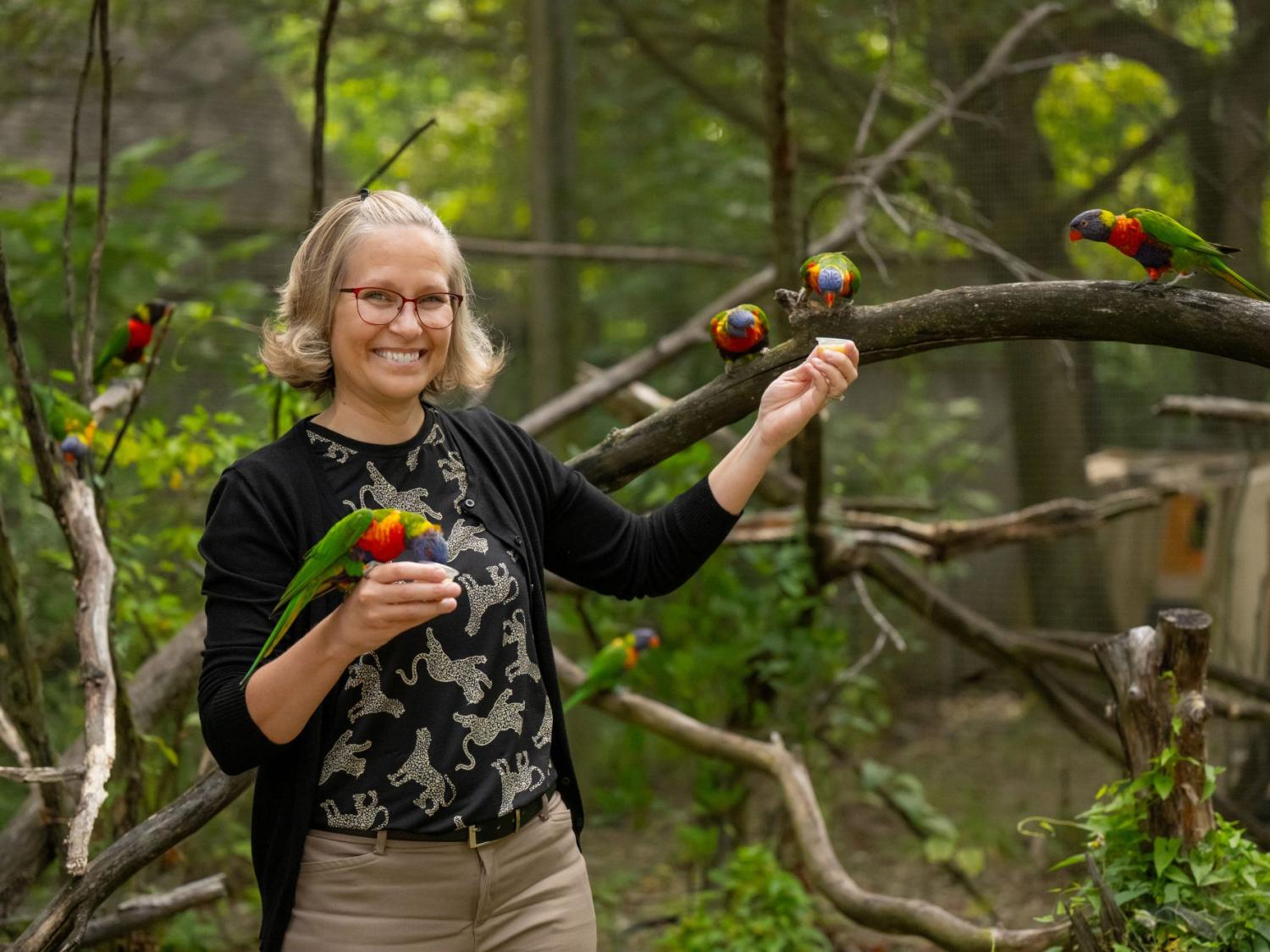 Penn State Behrend alumna Melissa "Roo" Kojancie poses with colorful birds in an exhibit space at the Erie Zoo, where she is the new president and CEO.