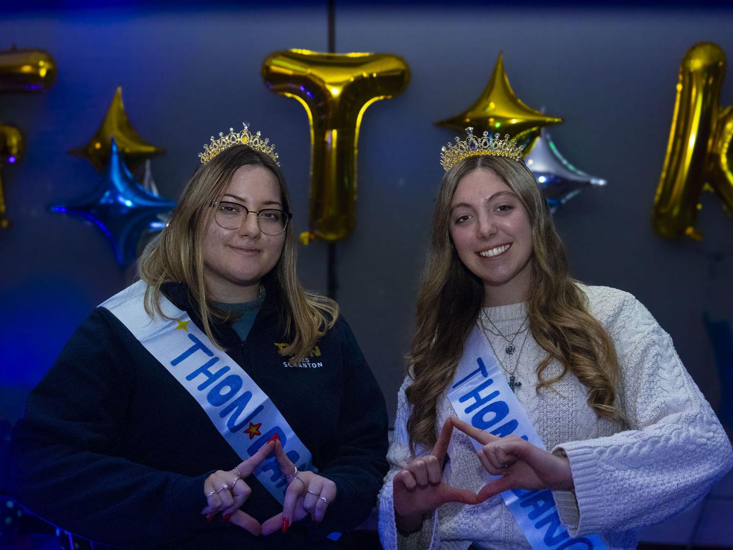 Scranton THON Dancers, Alexis Colasurdo and Airiana Scarfo stand side by side making the Four Diamonds hand symbol, with illuminated “FTK” letters glowing in the background.