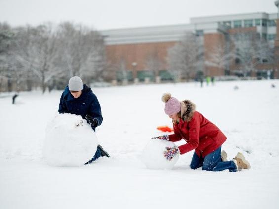 Two individuals roll snow to build a snowman