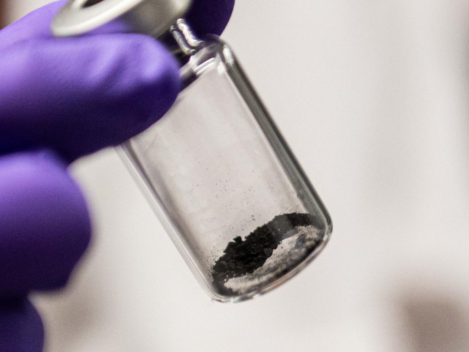 A gloved hand holds a vial with dust