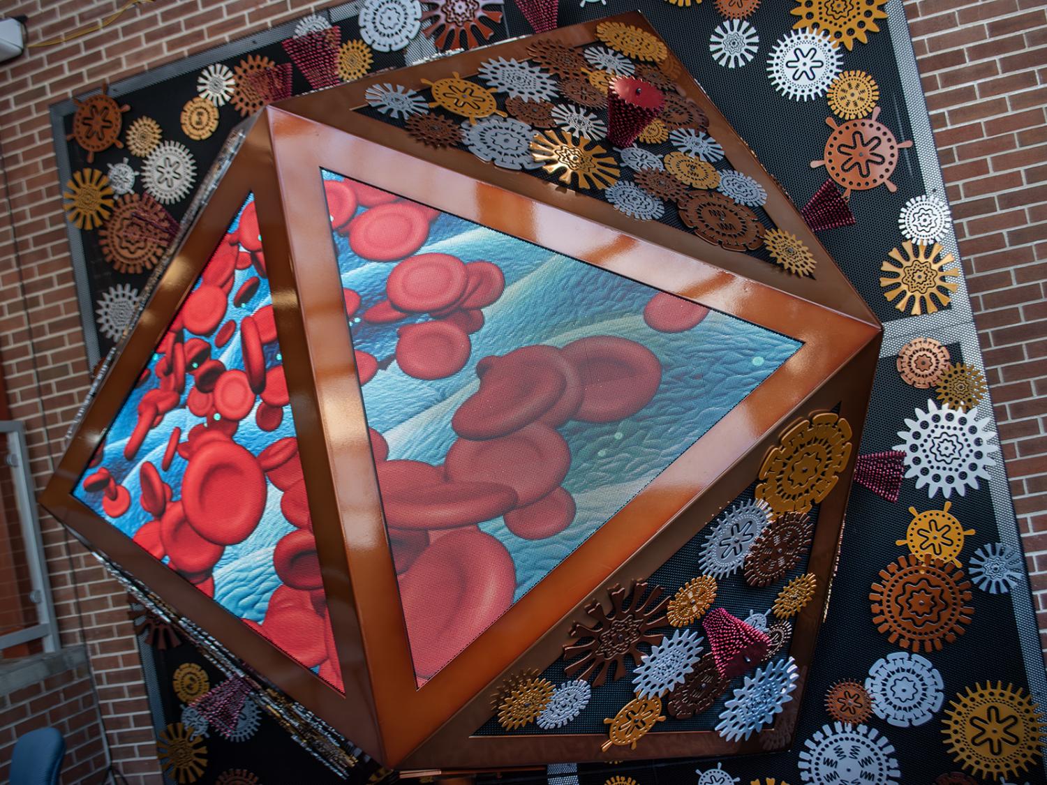 An aluminum sculpture, designed to mimic the structure of some viruses, with LED screens featuring visualizations related to virus research