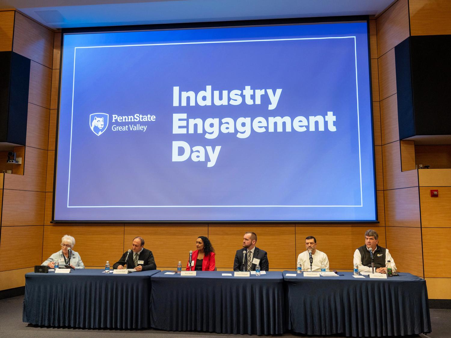 Six panelists sit at a table in front of a screen that says "Industry Engagement Day."