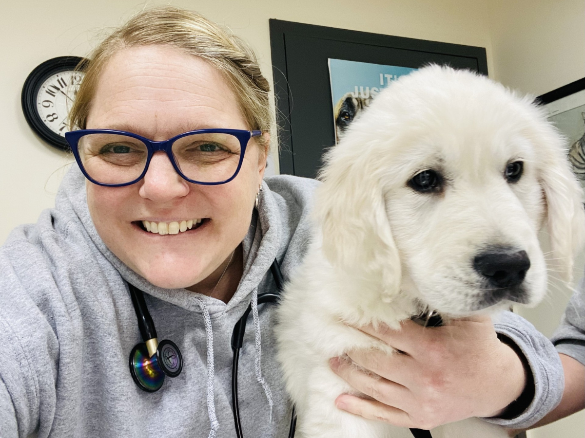 Jennifer Koehl smiling with her arm around a white and fluffy puppy