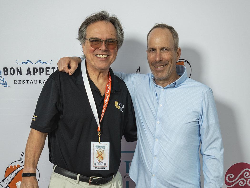 Two men standing side by side with one's arm draped around the other