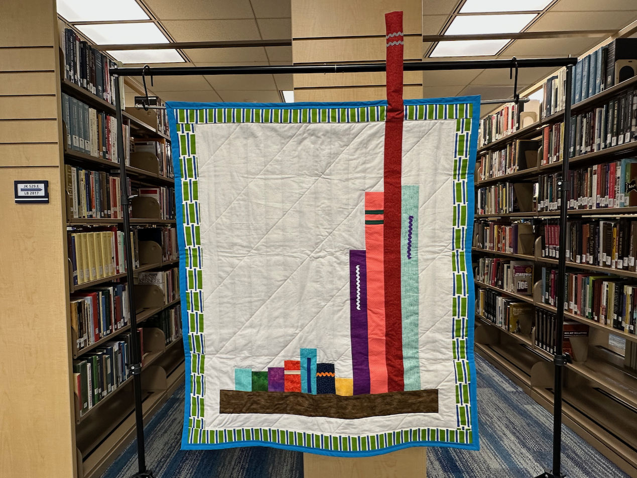 photo of hanging quilt showing bar chart of yearly data represented as book spines on a shelf