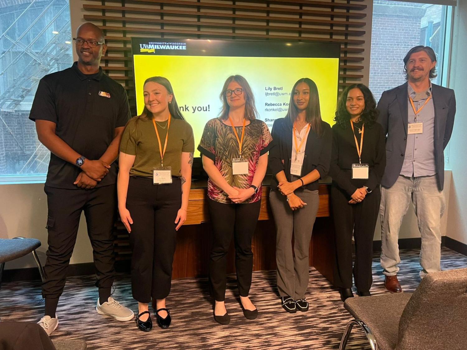 people who presented research stand in front of a screen