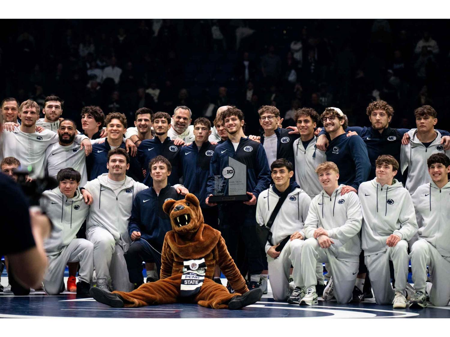 The Penn State wrestling team, consisting of a couple dozen men in blue and white uniforms, pose around the Nittany Lion for a photo