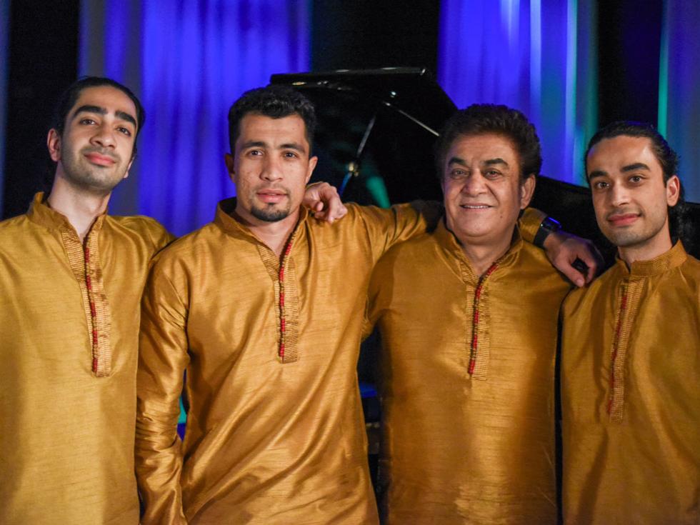 Four men of color wear traditional Afghan tunics and stand shoulder to shoulder.