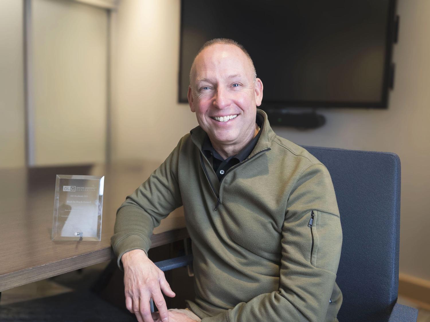 Fred Aebli sitting, with a crystal award plaque on the table next to him