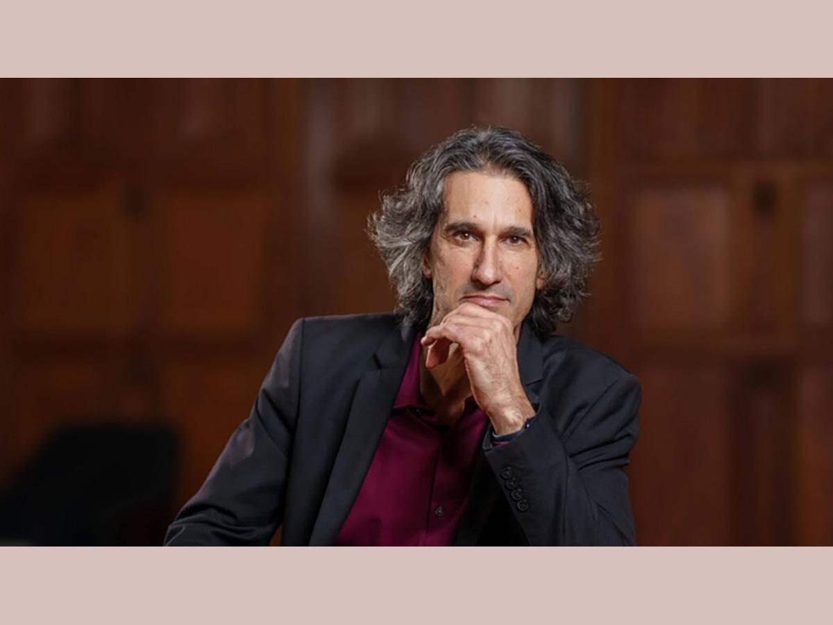 Agustín Fuentes wearing blue blazer and mauve shirt with hand resting on chin