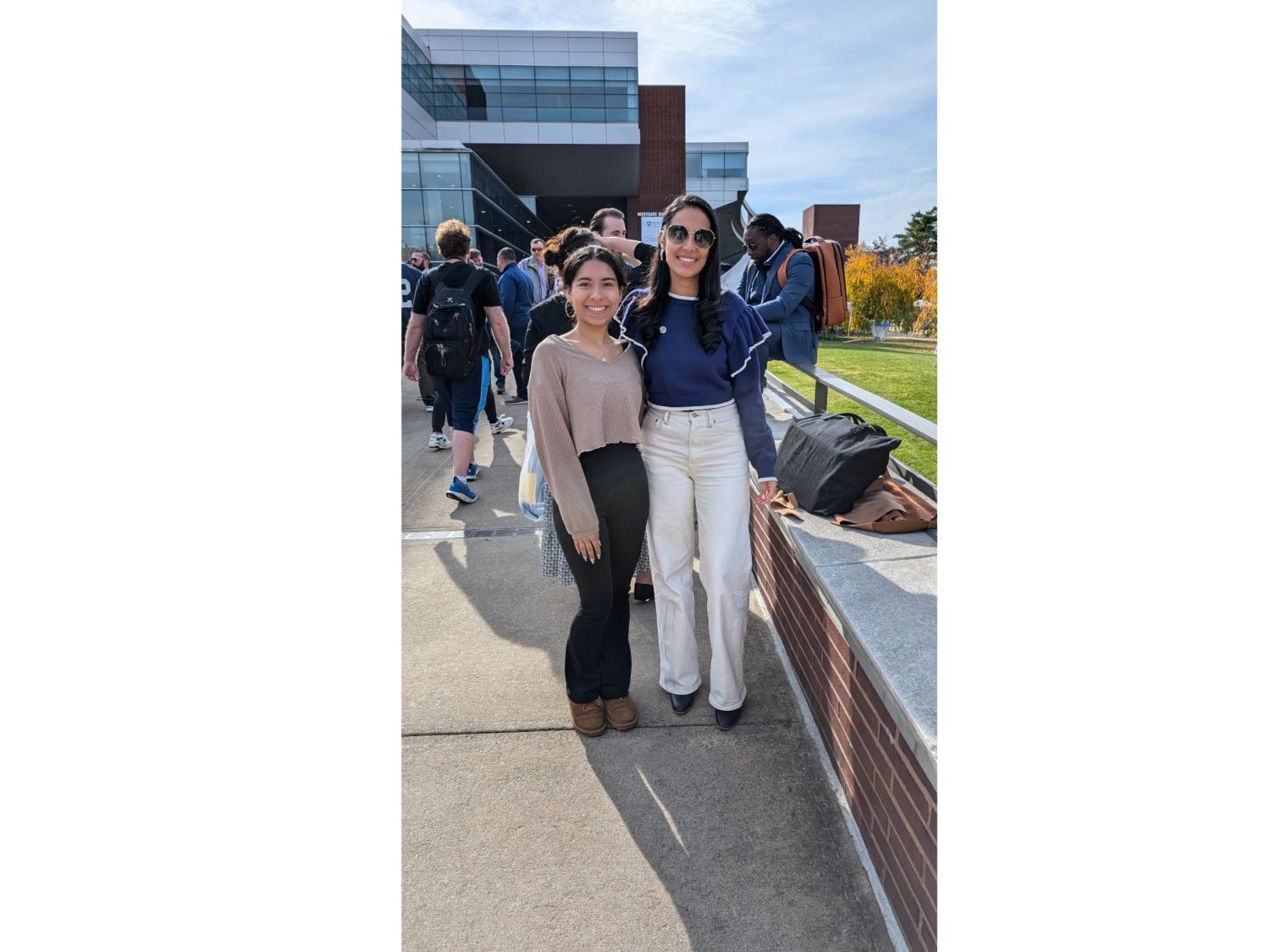 two dark-haired people stand on bridge leading to campus building