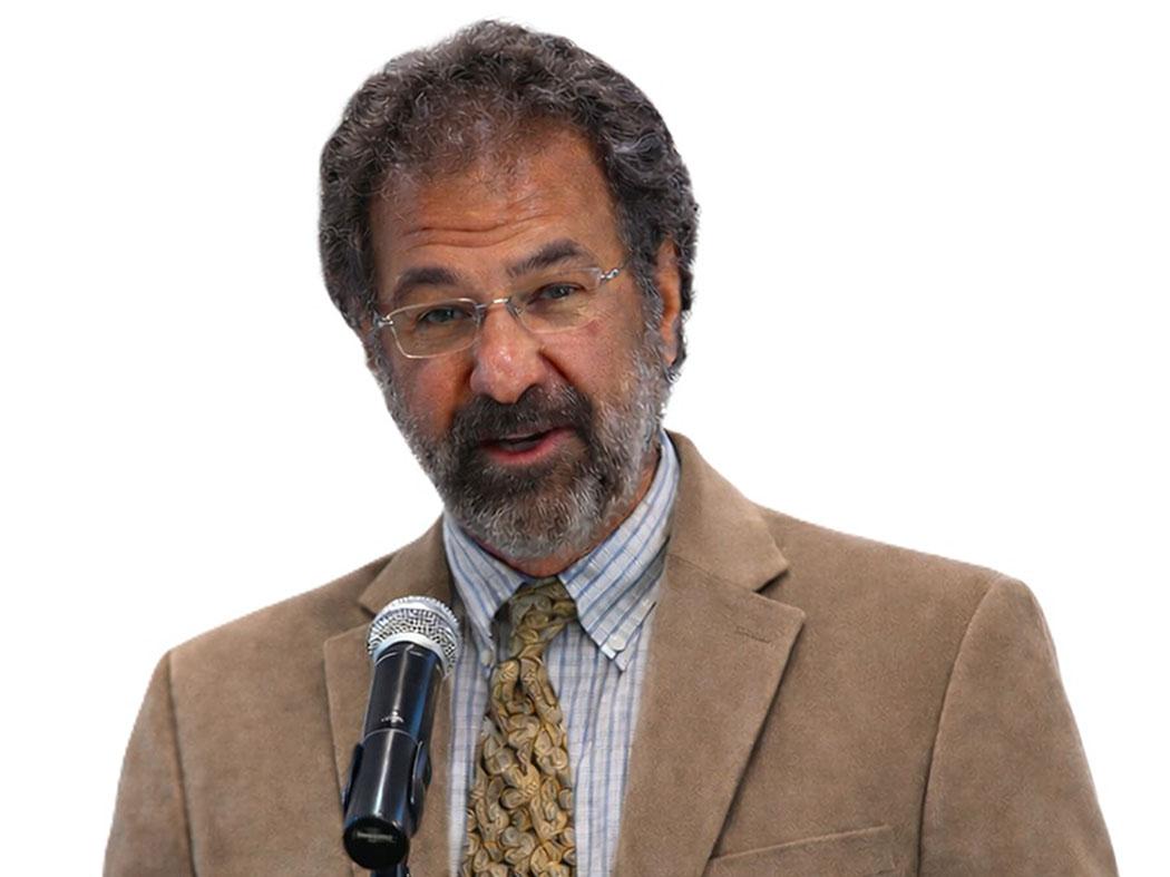 Man with curly graying hair standing behind a microphone