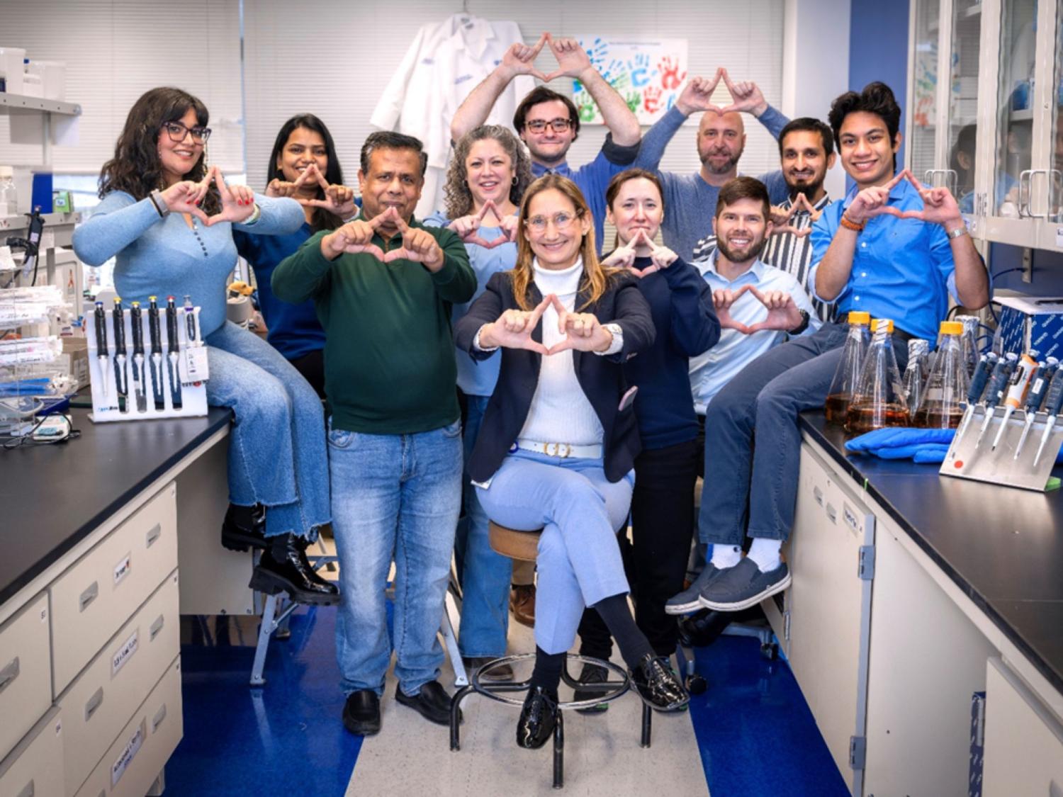 10 people in a lab pose for a photo shaping their fingers into a triangle