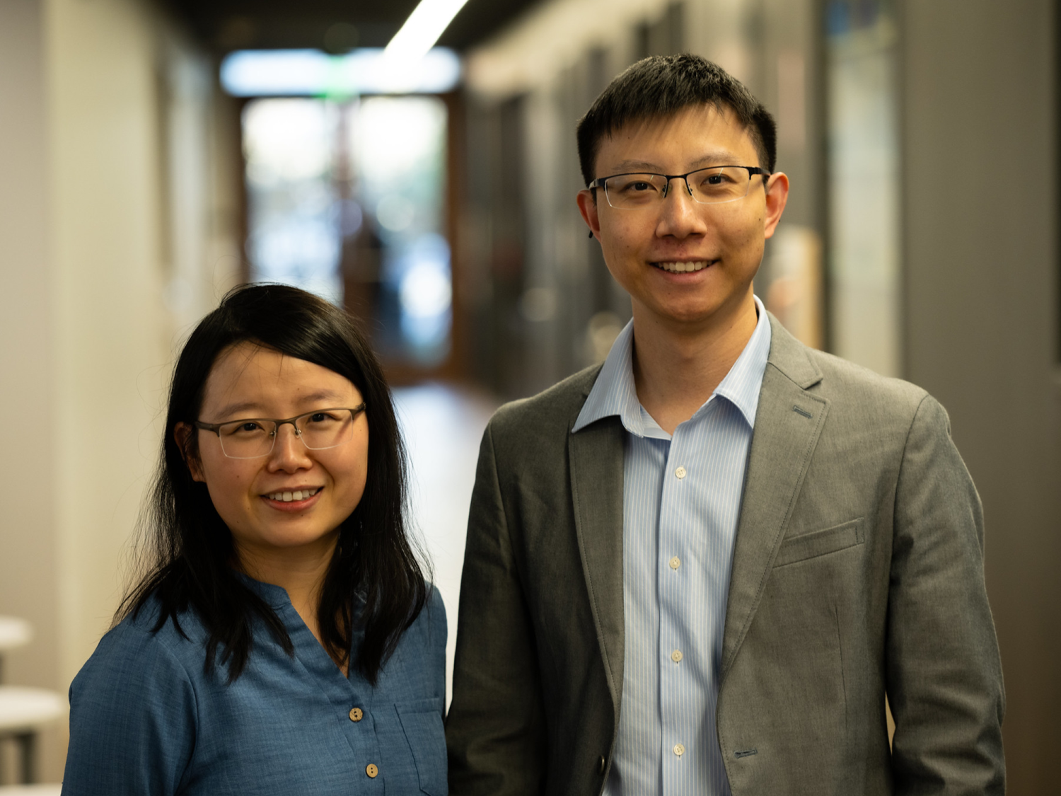 Two people stand in a hallway and smile at the camera