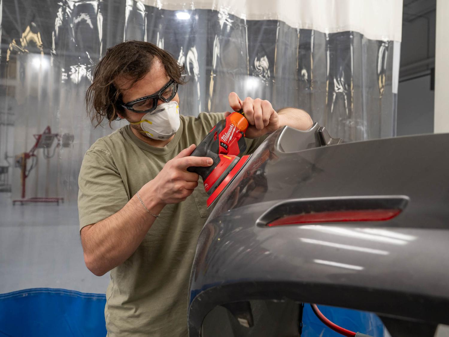 A man operates an orbital sander on a vehicle