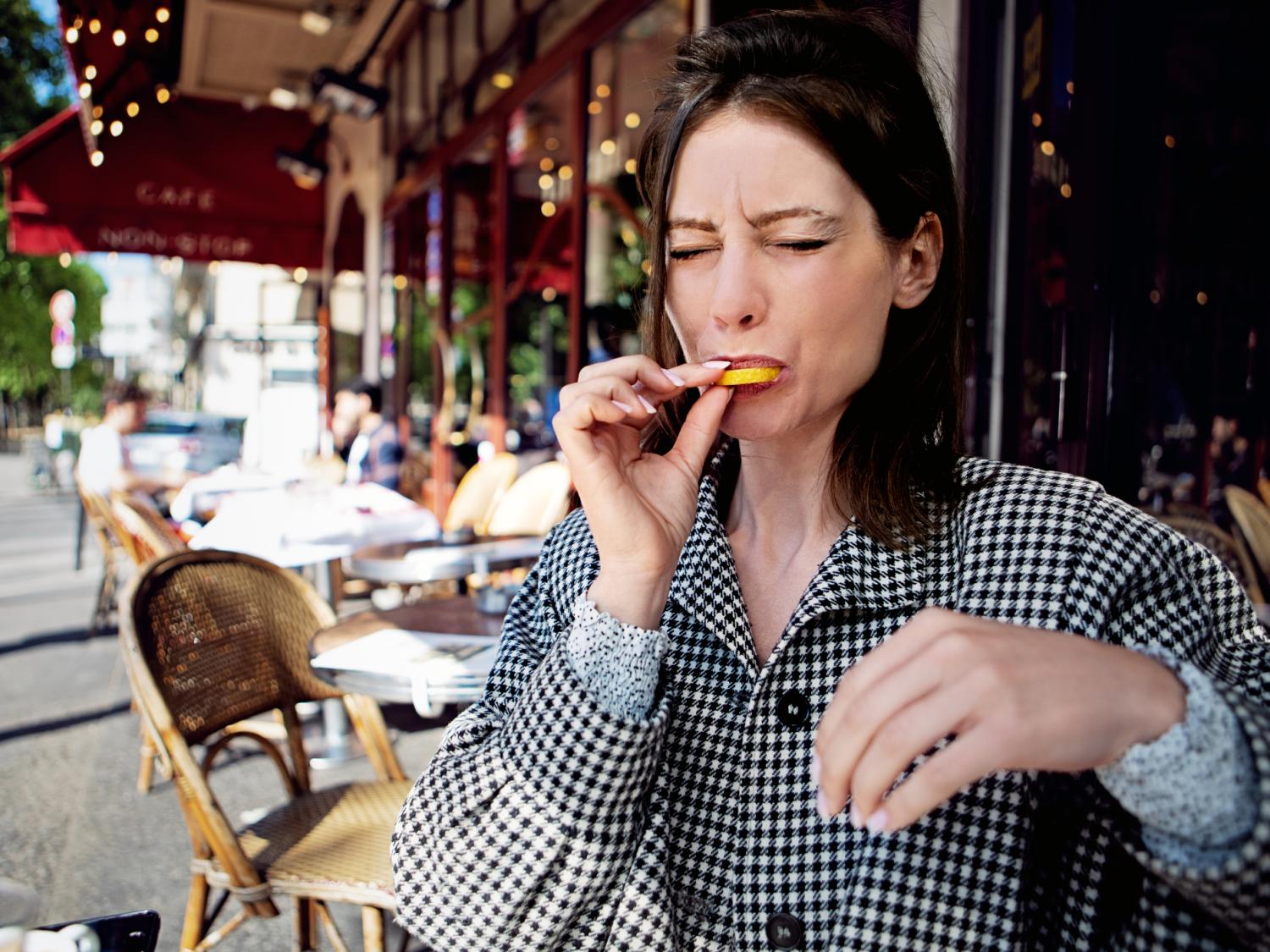 Person at an outdoor café, biting into a lemon slice