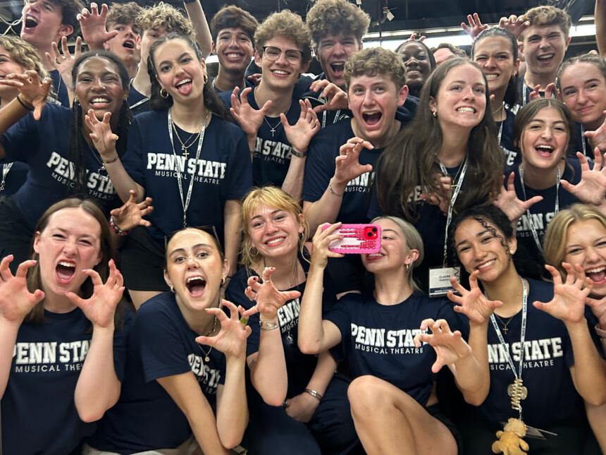 A group of high school students wearing Penn State t-shirts make claws with their hands while smiling for the camera