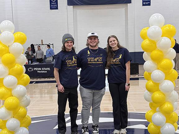 Photograph of three people standing on a gymnasium floor at Penn State Hazleton, flanked by yellow and white balloon columns.