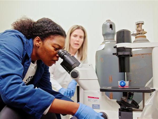 Student looking through microscope with faculty member in background
