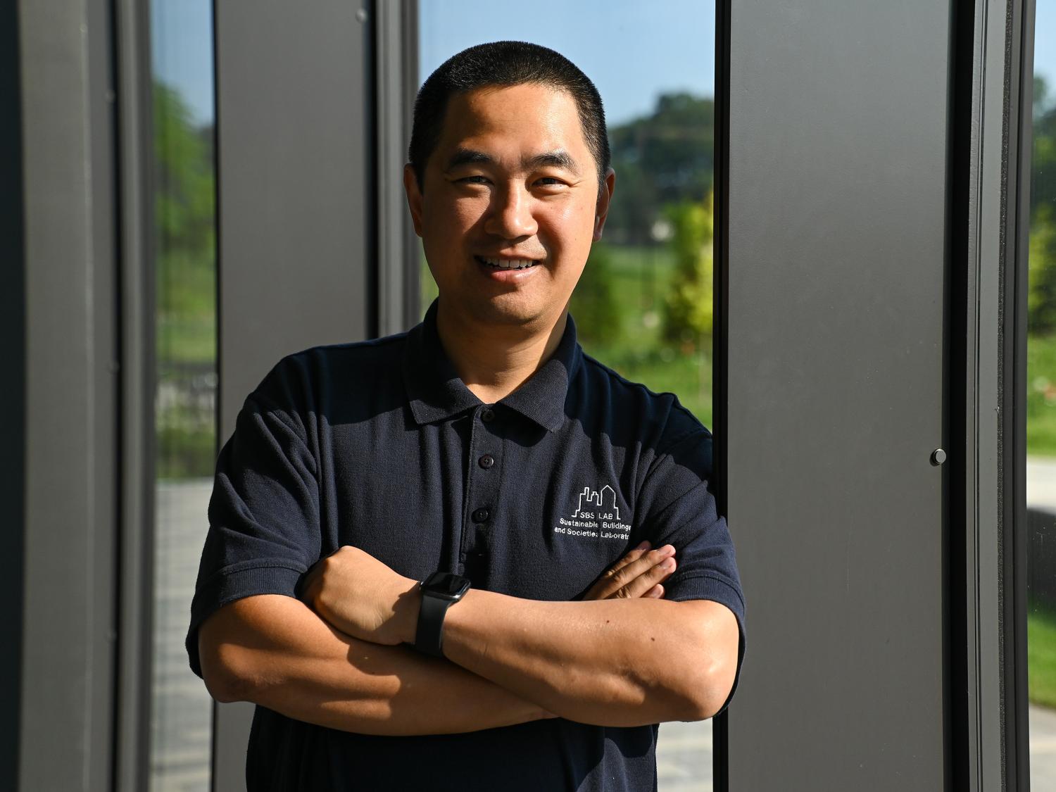 Wangda Zuo poses for a portrait with his arms crossed in front of a window.