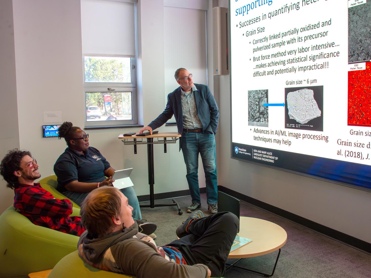 Jon Schwantes stands in front of a projector screen, teaching a group of students.  