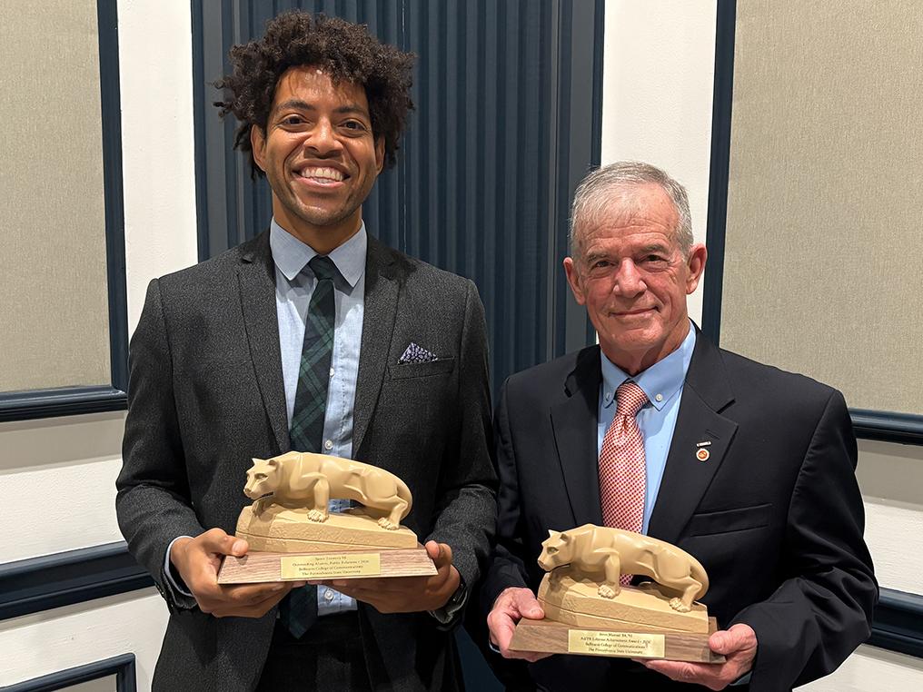Two men standing side by side holding small statues