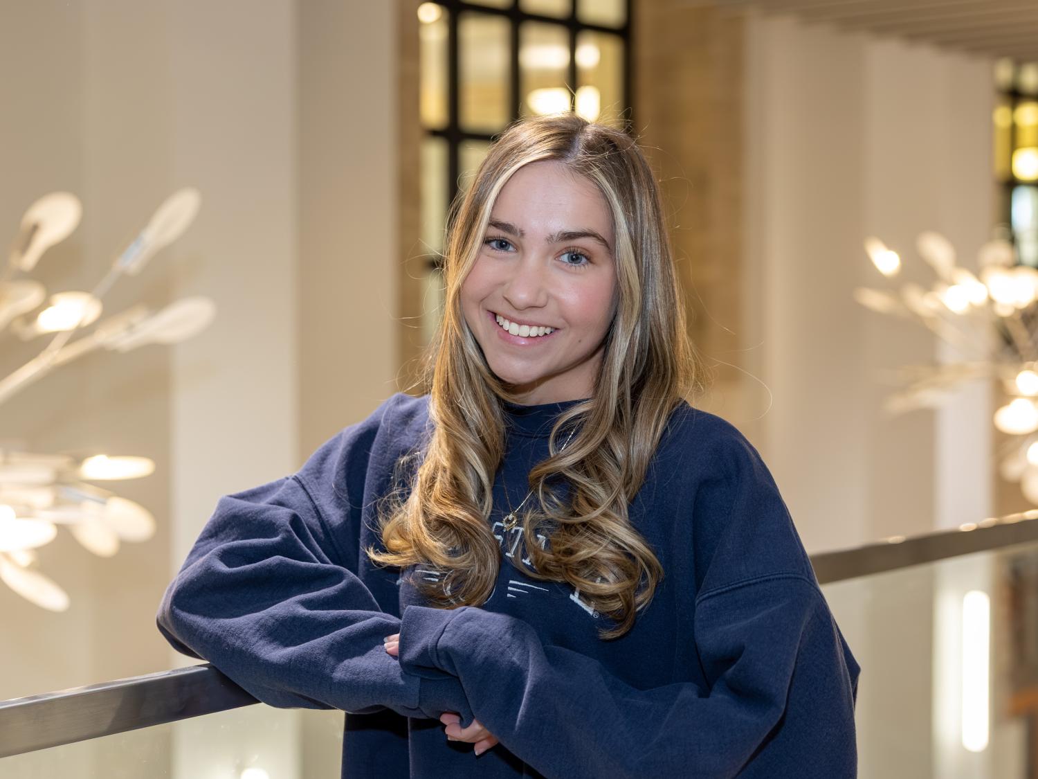 Jessica Amatrudo wears a navy blue Penn State sweatshirt while leaning against a glass banister in Pattee Library.