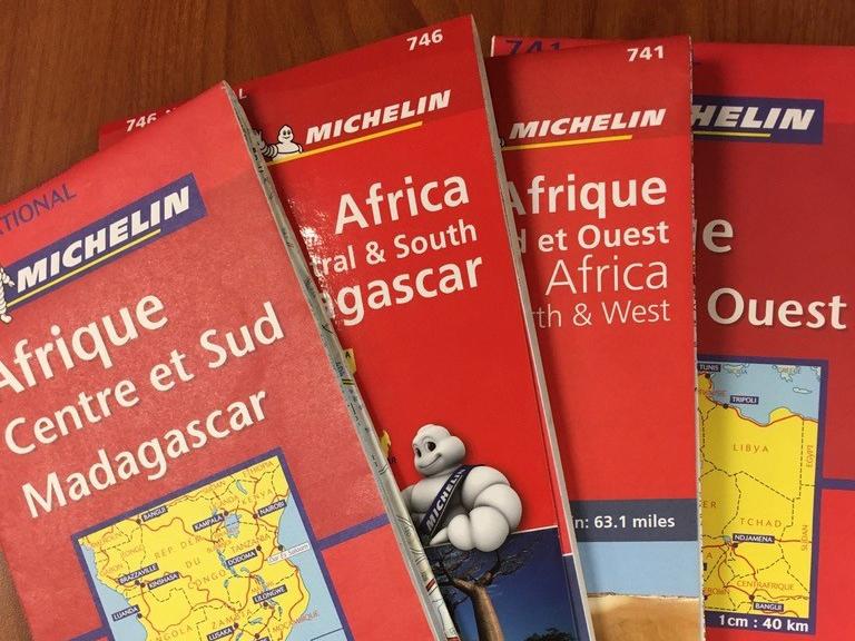 Four folded Michelin maps of Africa fanned out on a desk.