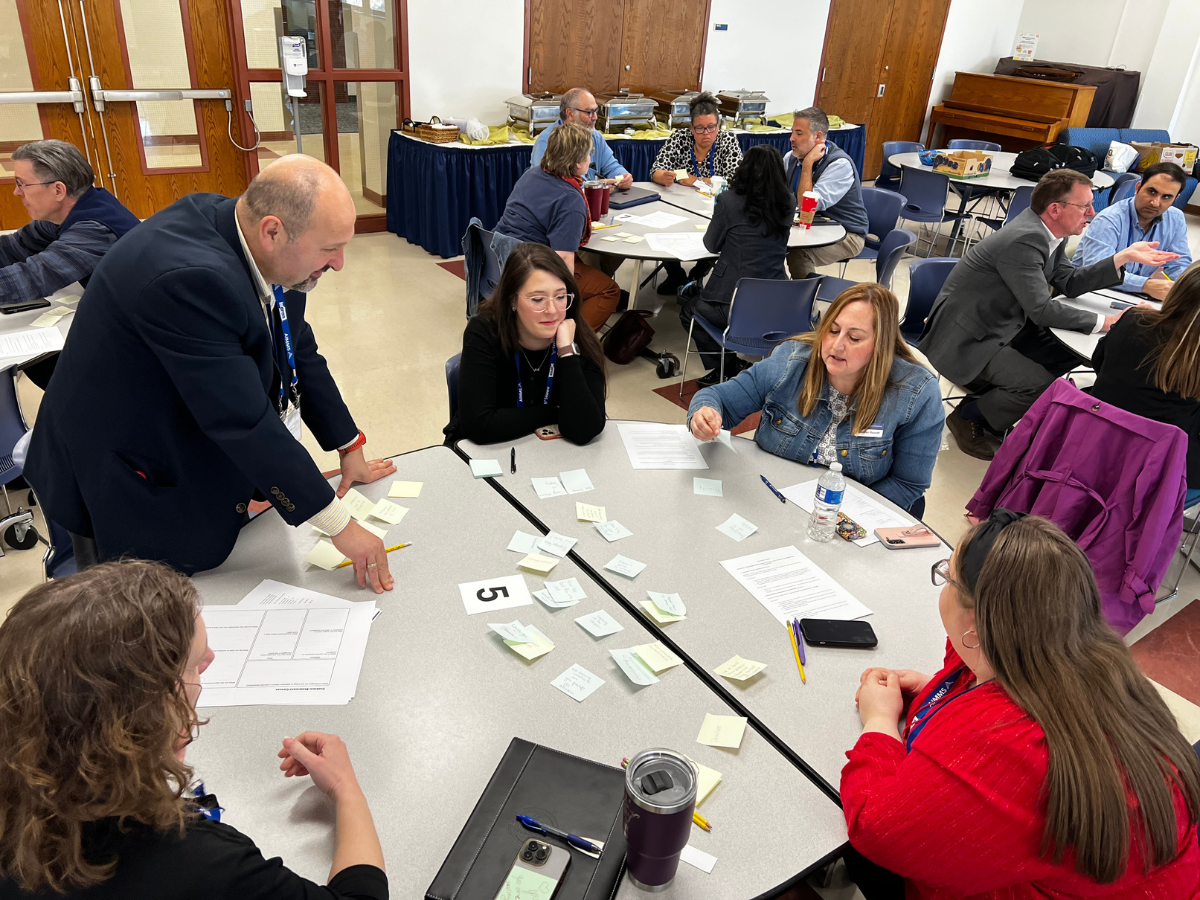 Abdullah Konak stands at a table full of people at a workshop.