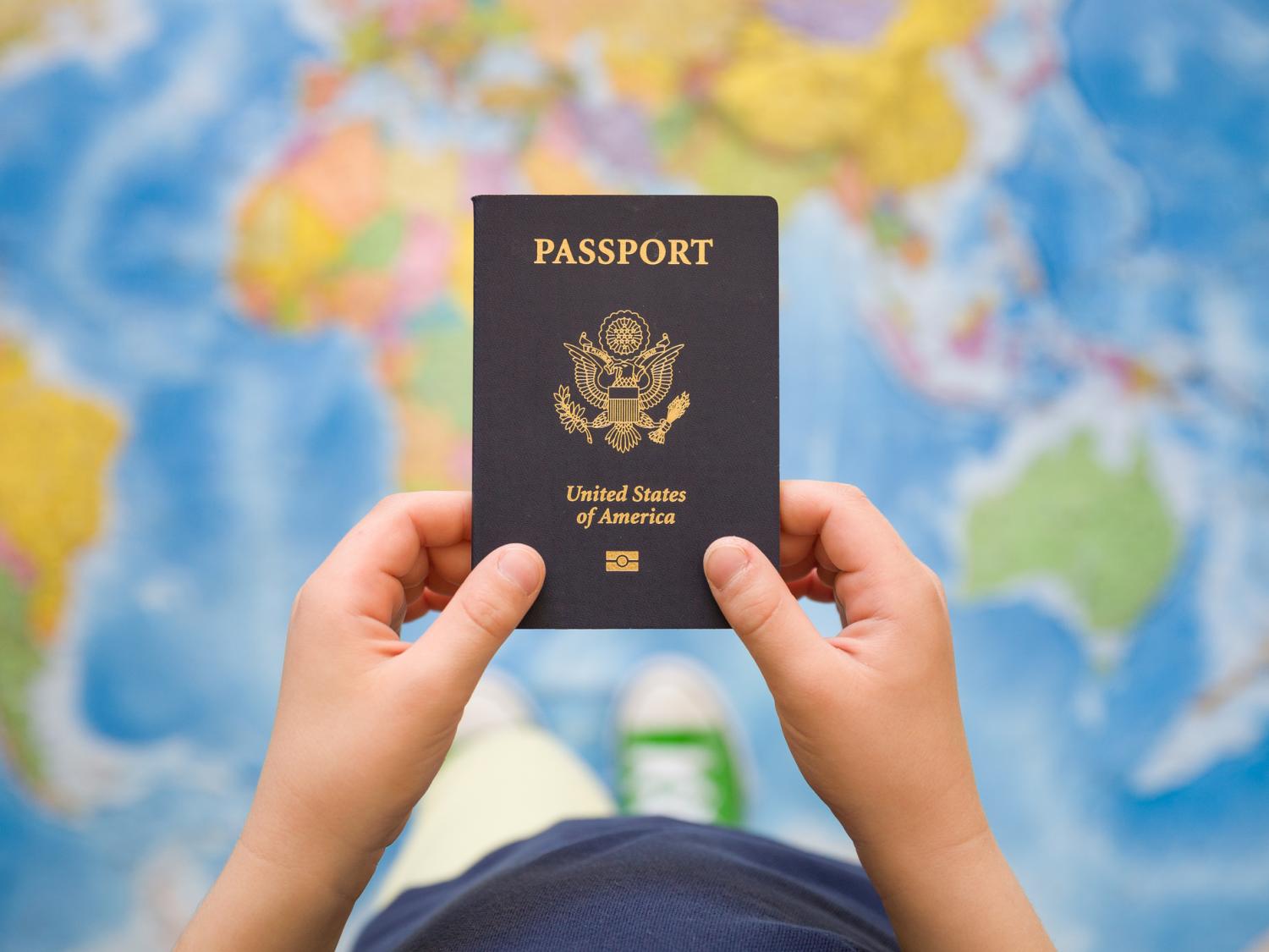 A child's hands holding a U.S. passport, with a map of the world in the background