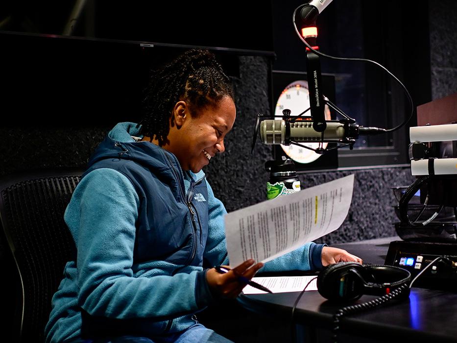 A student sitting in front of a microphone makes edits on some paper