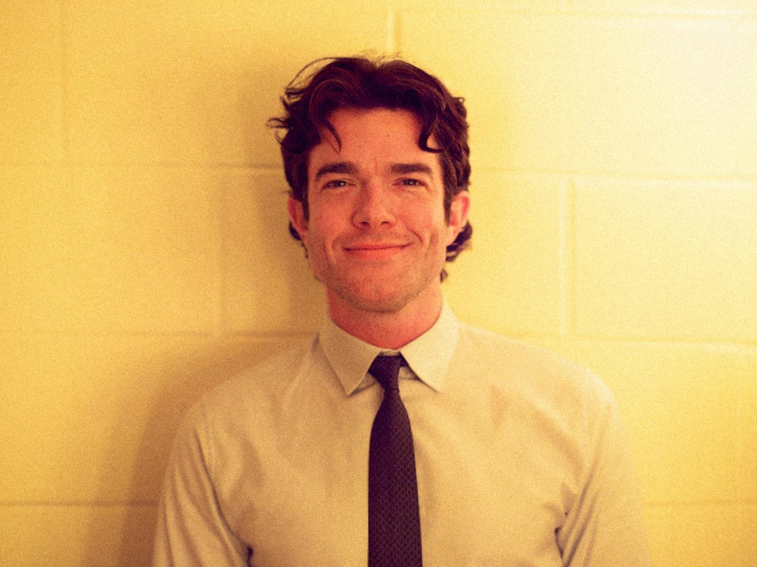 John Mulaney in front of a yellow cinder block wall