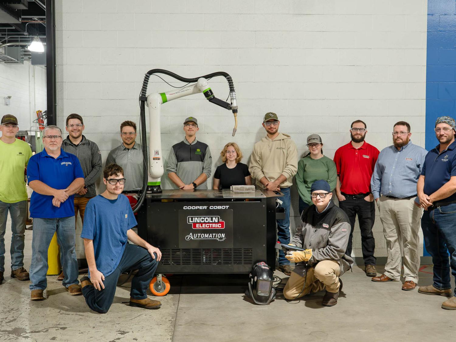 A group of about a dozen students gather round an industrial robot