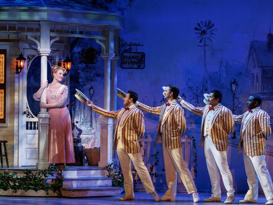 Four men in striped jackets serenade a woman on a porch.