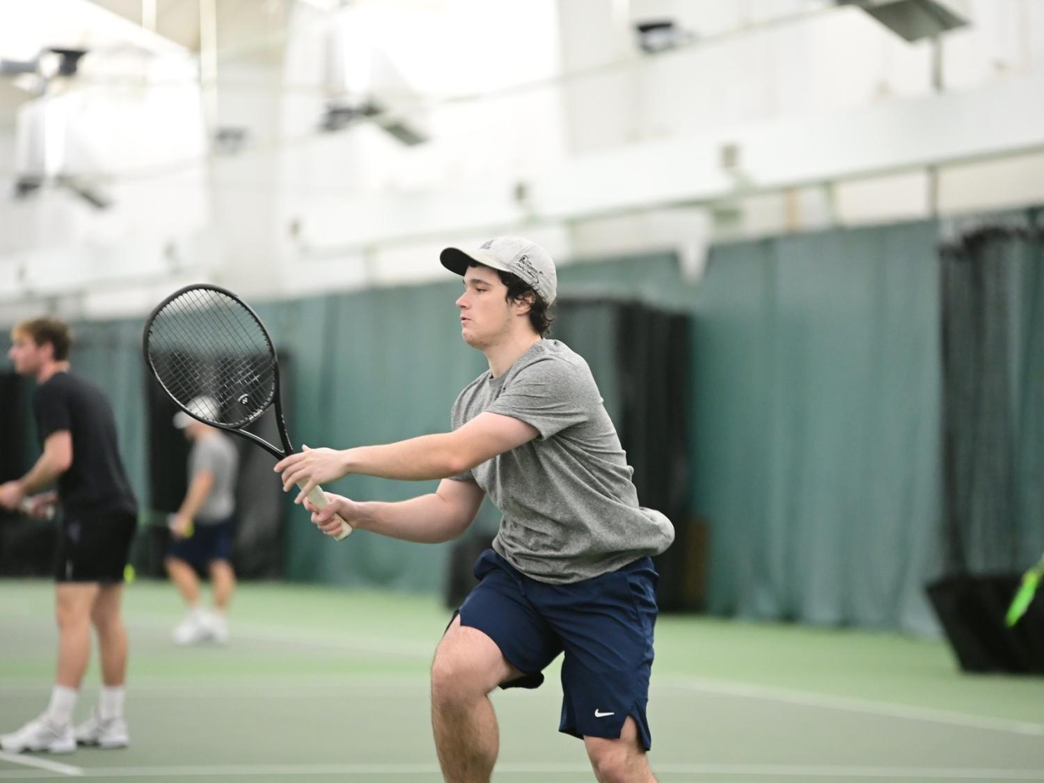 A member of the Penn State Behrend men's tennis team hits the ball during an indoor match.