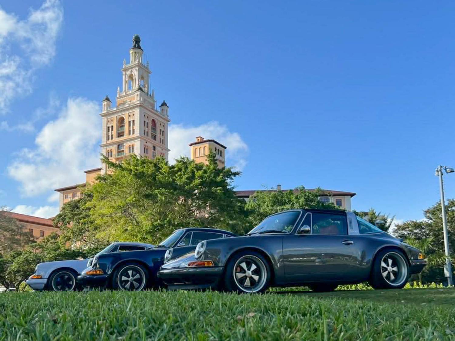 A view of luxury automobiles displayed outside a tall hotel on the grass