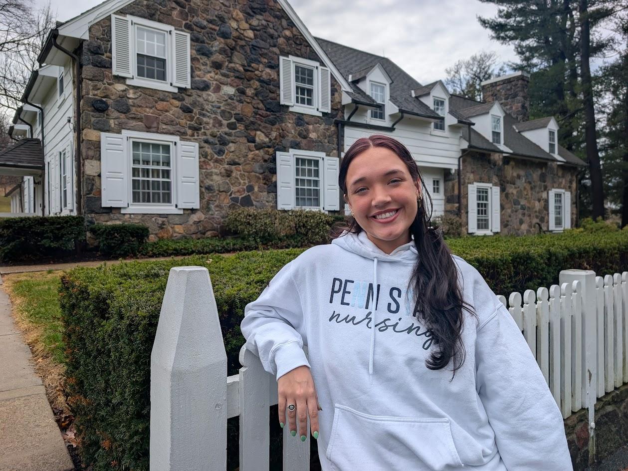 Penn State Behrend student Mya McElhinney leans on a fence in front of Glenhill Farmhouse.