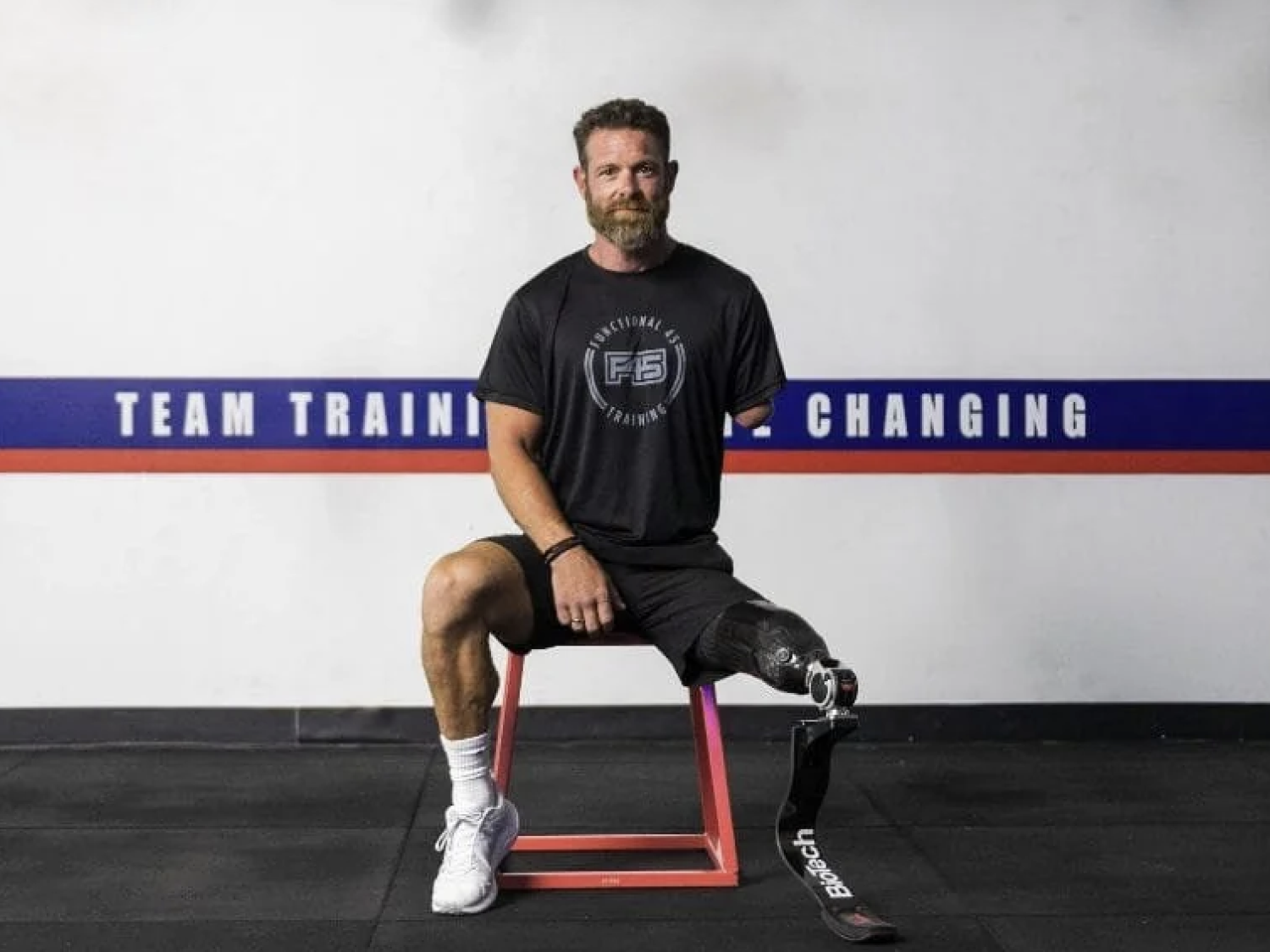 A photo of Galloway sitting on a stool and wearing shorts and a t-shirt. His prosthetic limbs are visible.