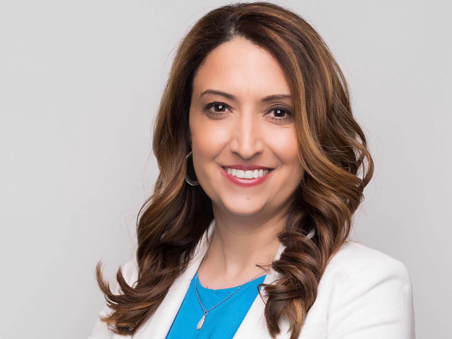A head and shoulders photo of a smiling Donna Palumbo, who is wearing a white blazer over a blue blouse.