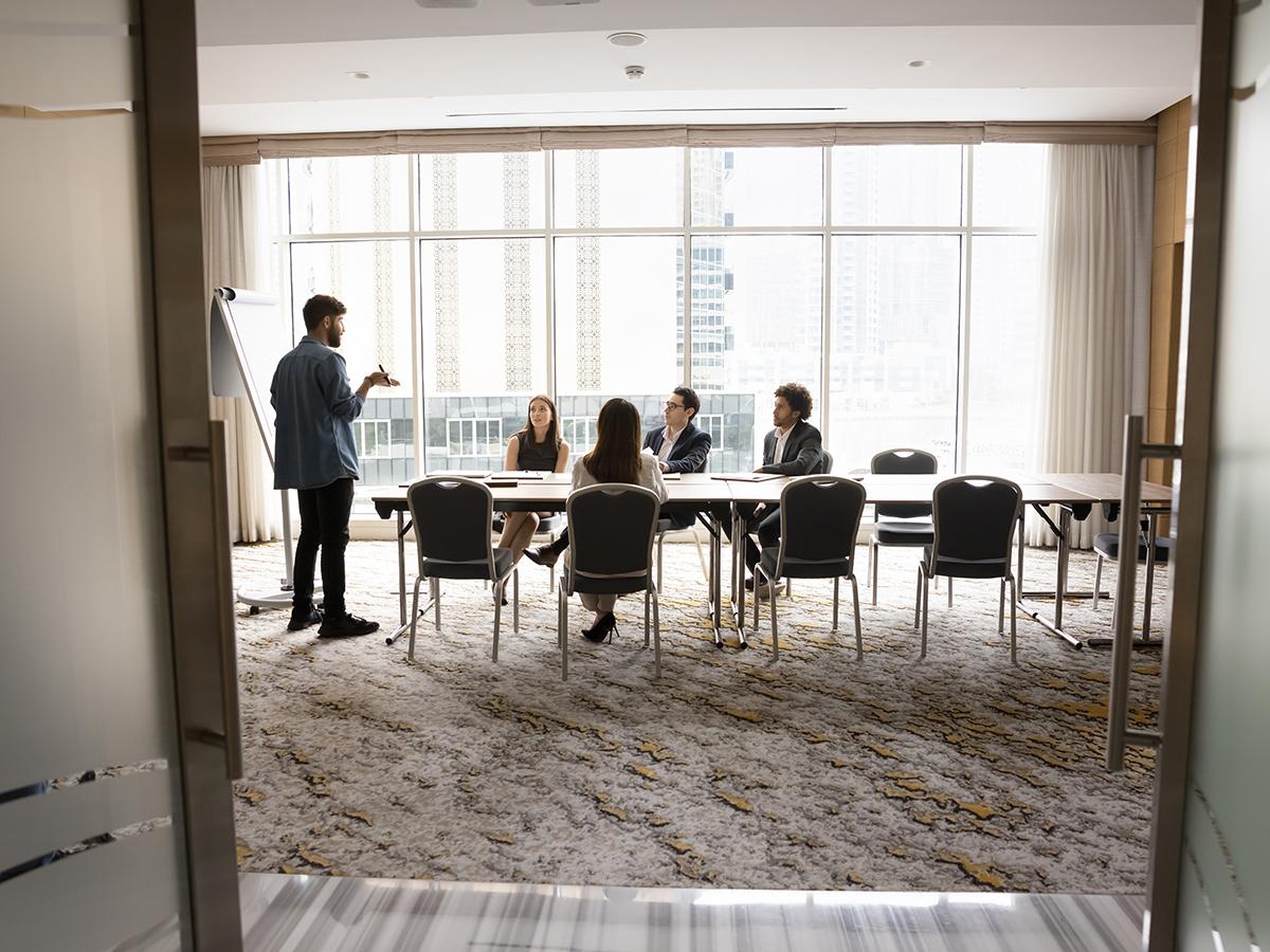 An instructor leads a small professional training session with participants seated around tables in a bright conference room.
