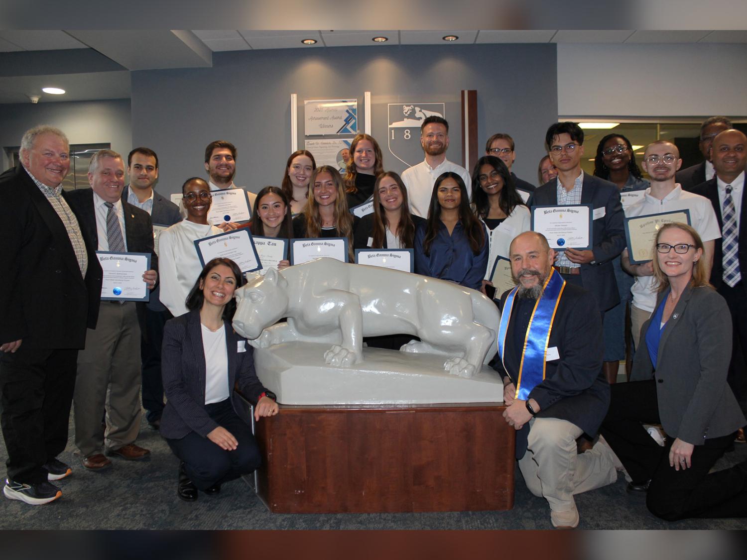Newly inducted members of business honor societies and faculty pose with the Lion statue in Olmsted Building