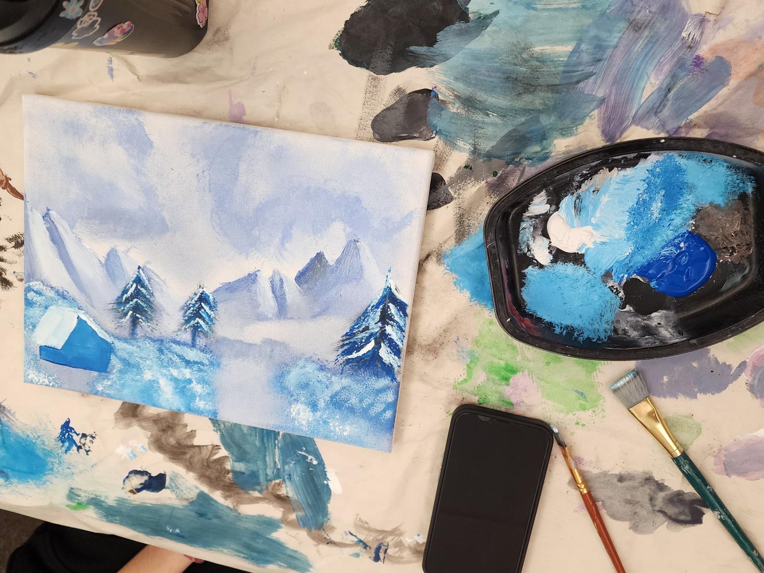 A student's painting on a desk, with paint and paintbrushes to the side of the artwork