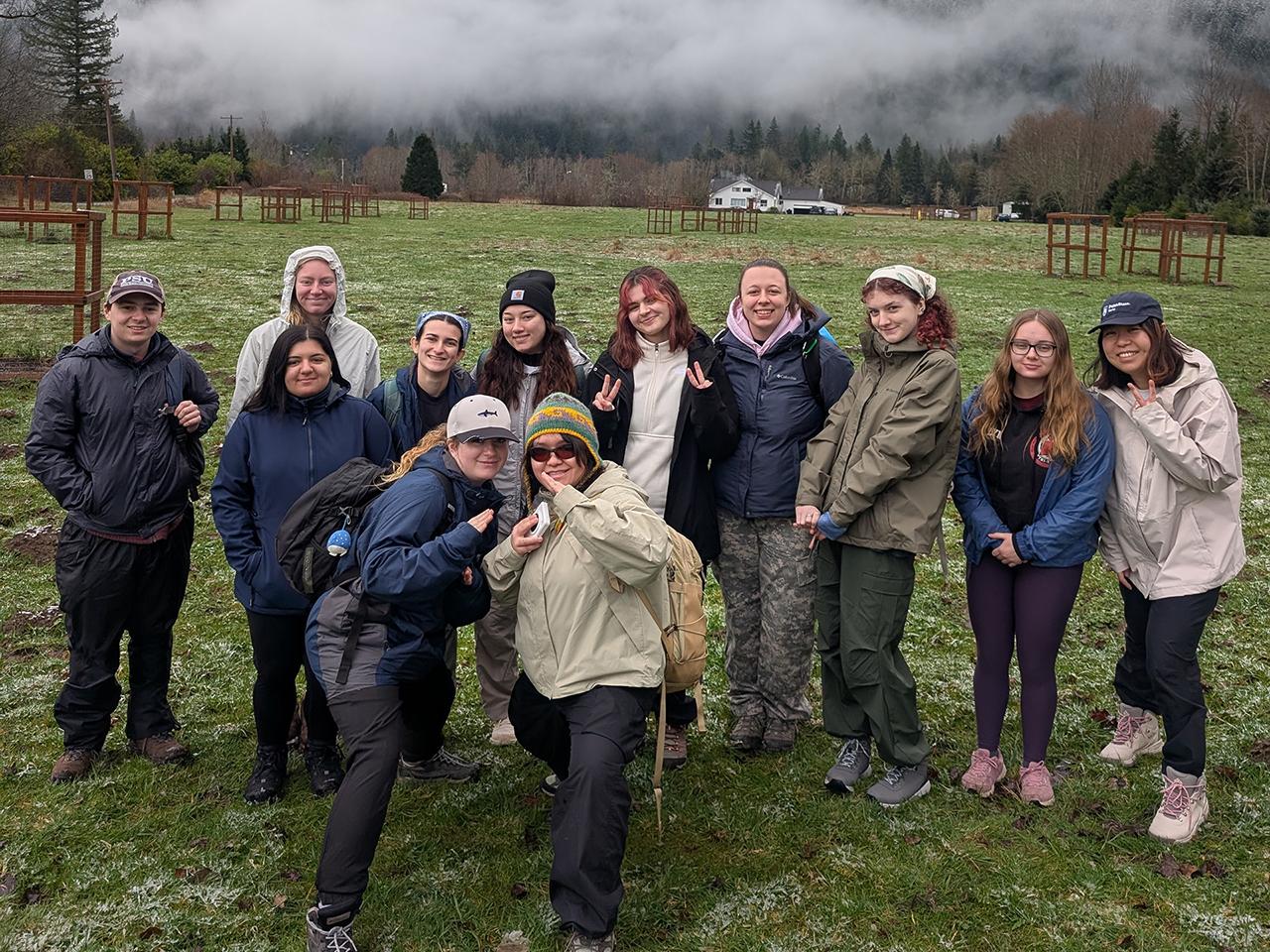 A group of students wearing winter coats and hats poses in front of a large, snowy mountain