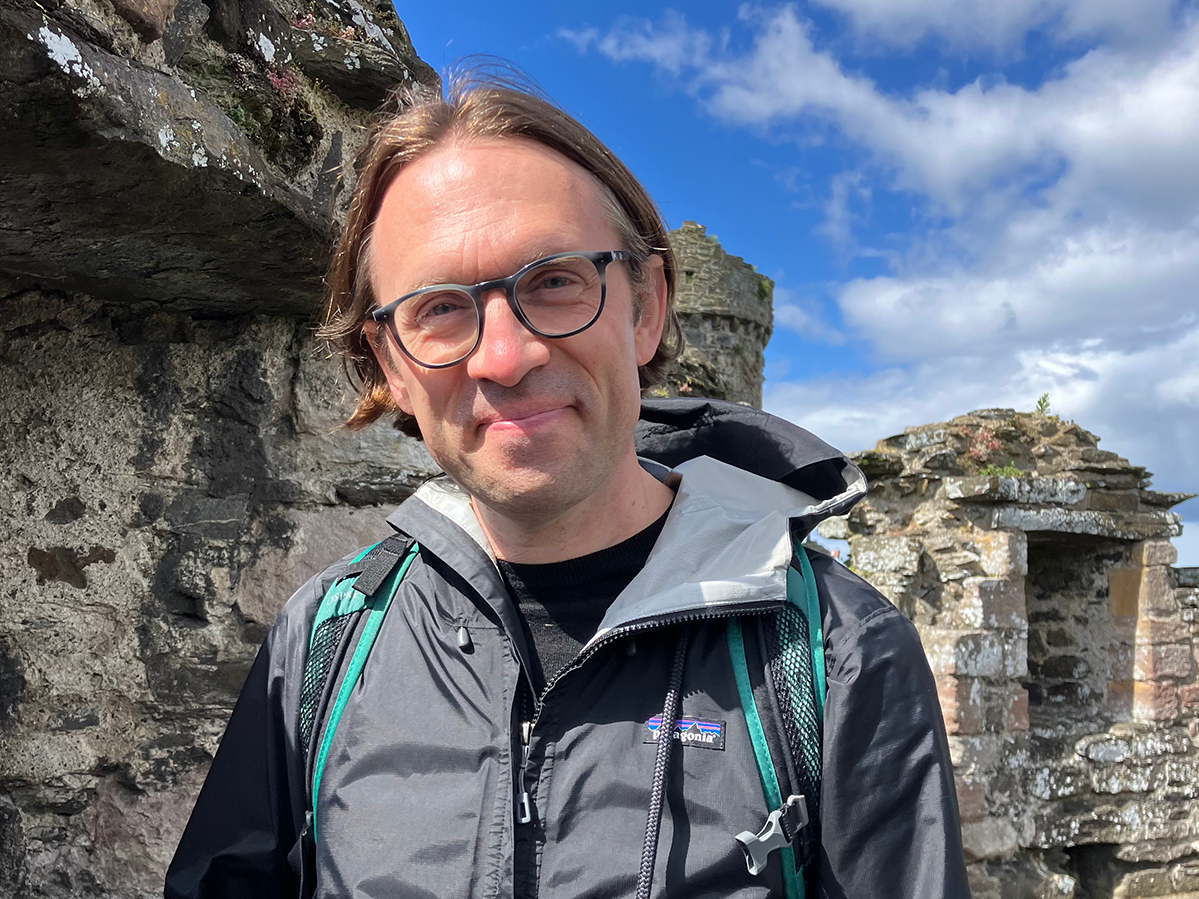 A man wearing glasses and a windbreaker pictured atop the remains of a castle