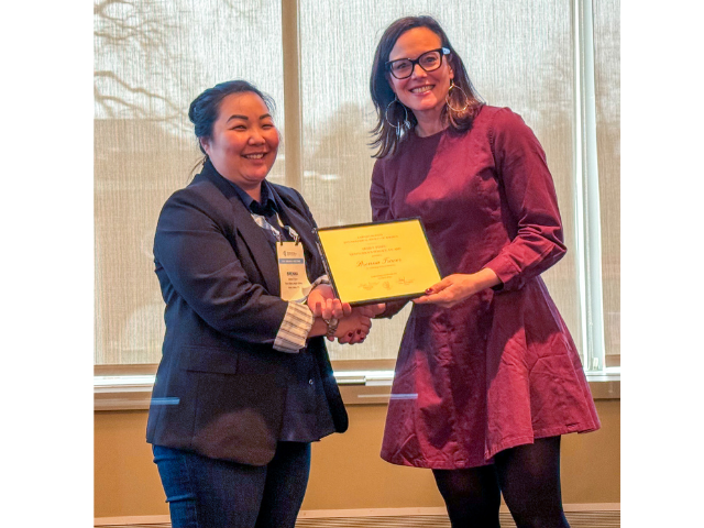 two women stand next to each other smiling while holding a plaque award