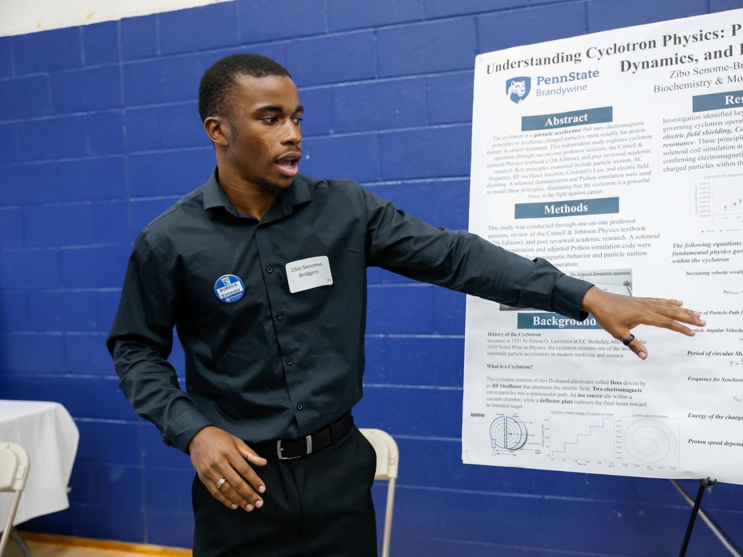 student talking about his work while gesturing to a poster he made about proton radiation